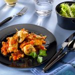 Involtini di pesce spada: un secondo piatto estivo 1 su tavolo apparecchiato, piatto nero con involtini di pesce spada e un bicchiere di acqua e di vino bianco e in una ciotola insalata verde.