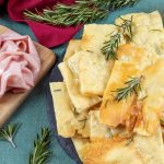 Scrocchiarella: la pizza romana croccante e deliziosa 1 vassoio con pizza bianca scrocchiarella e rosmarino, vassoio con mortadella accanto