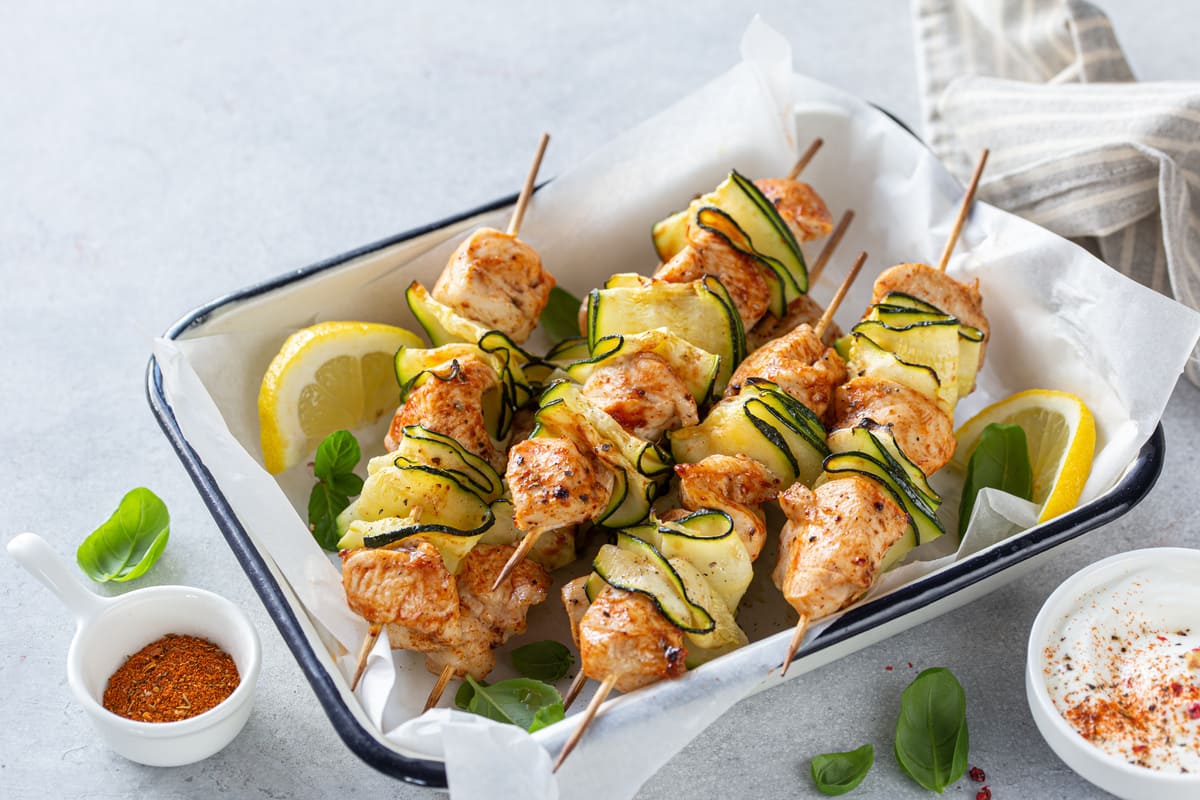 Spiedini: le migliori ricette di carne, di pesce o vegetariane 1 Spiedini di carne di pollo con zucchine e patate al forno, serviti in una teglia bianca con limone e salsa allo yogurt.