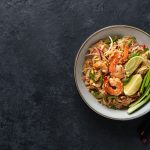 Pad thai: come preparare il famoso piatto thailandese in casa 1 su sfondo nero un piatto bianco con un pad thai con gamberi, tofu e noodles. Accanto mezzo limone