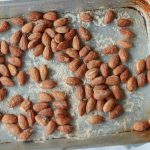 Mandorle tostate: uno snack sano e versatile 1 primo piano di mani che tengono una teglia da forno con carta da forno e mandorle tostate