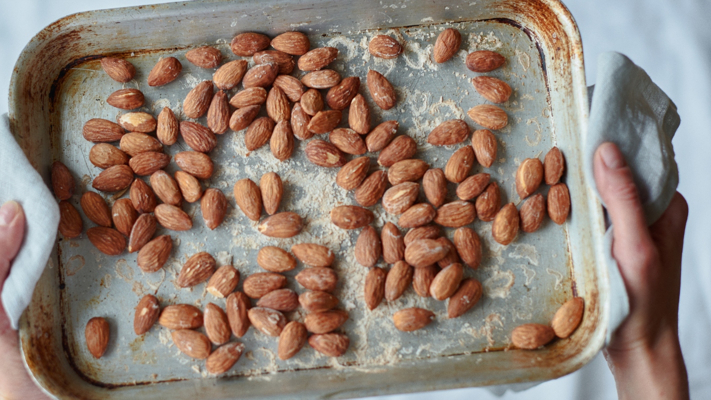 Ricette con le mandorle: tante idee gustose da provare 26 primo piano di mani che tengono una teglia da forno con carta da forno e mandorle tostate