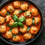Gnudi: un primo piatto goloso con ricotta e spinaci 1 su tavolo da cucina nero primo piano di una padella con gnudi al pomodoro e attorno foglie di basilico e pepe nero