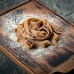 Tagliatelle con farina di castagne: un primo piatto autunnale saporito 1 Su tavolo di marmo, tagliere con tagliatelle con farina di castagne appena fatte e farina