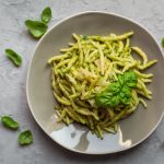 Trofie al pesto, un delizioso primo piatto della Liguria 1 su piano di lavoro di marmo, piatto grigio con le trofie al pesto e foglie di basilico