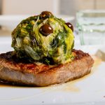 Scarola in padella, la ricetta romana di un contorno sano e gustoso 1 su tavolo bianco: una fetta di carne di manzo con scarola in padella sopra a forme di palle con olive nere di Gaeta
