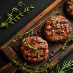 Hamburger di carne fatti in casa: la ricetta per renderli morbidi e gustosi 1 Su tavolo di legno, tagliere con 3 hamburger di carne , pepe nero, erbe aromatiche