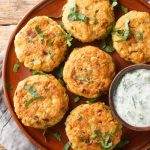 Hamburger di ceci: una ricetta vegetariana semplice 1 su tavolo di legno, canovaccio e sopra un piatto marrone con hamburger di ceci e prezzemolo e un contenitore con salsa allo yogurt e 2 fette di limone