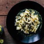 Pasta con spinaci: un primo piatto sano e leggero 1 su tavolo di legno, piatto nero con pasta con spinaci freschi. A sinistra una pianta con fiori