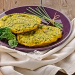 Frittata di spinaci 1 ricette con frittata: su tavolo di legno, canovaccio beige con sopra un piatto viola con frittata di spinaci, erba cipolline e una foglia di spinaci freschi