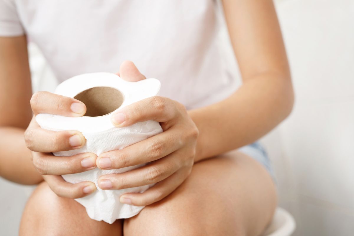 Rimedio immediato per andare in bagno: cosa fare (10-30 minuti) 2 una donna seduta sul water che stringe un rotolo di carta igienica