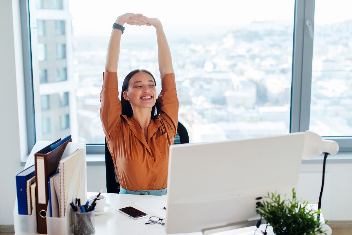Dormire con il mal di schiena: come riposare senza dolore 2 come dormire con il mal di di schiena: una giovane donna seduta in ufficio che fa stretching per la schiena