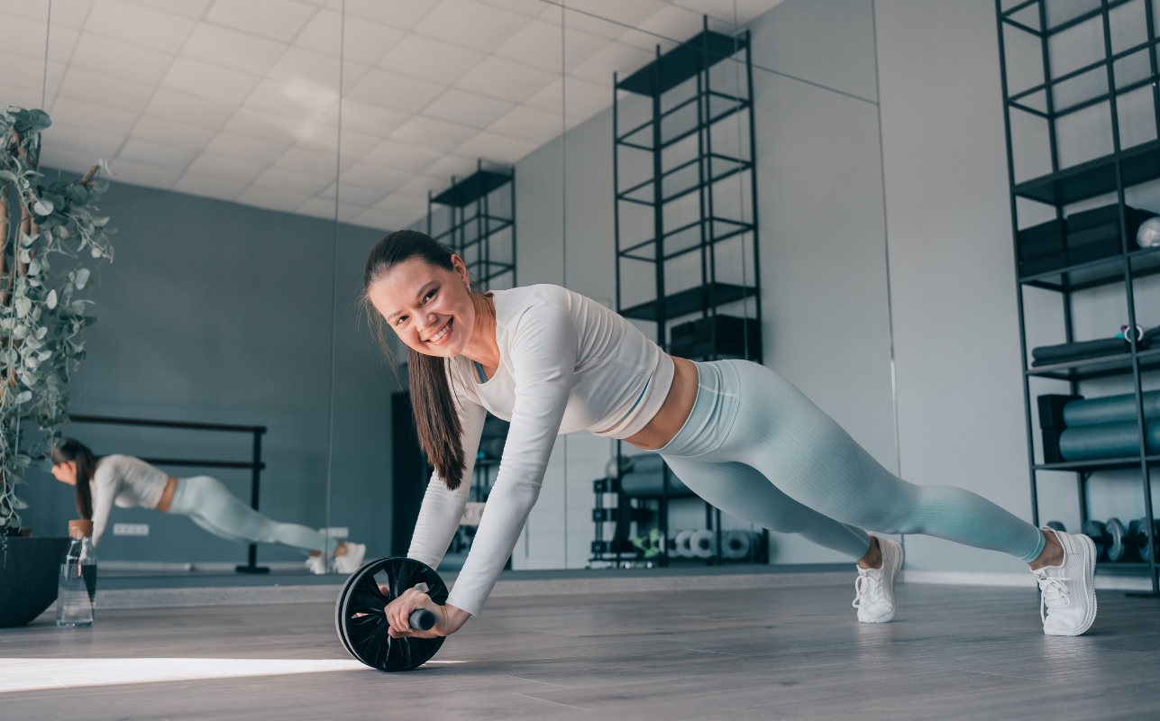 Donna sorridente si sta allenando gli addominali con la AB roller ABS ( ruota per addominali)