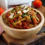 Fagiolini all'uccelletto: la ricetta toscana tradizionale 1 su tavolo, tagliere con ciotola in marmo con fagiolini all'uccelletto con alcuni fagiolini lavati e tagliati e dietro pomodorini