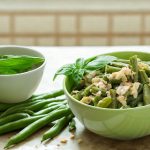 Fagiolini lessi: tempo di cottura e come condirli 1 su tavolo da cucina, ciotola verde con fagiolini lessi e parmigiano, accanto un'altra ciottola con basilico e a destra fette di pizza
