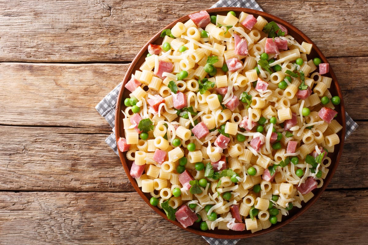 in primo piano un piatto di pasta con prosciutto cotto e piselli