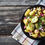 Insalata di patate: la ricetta di un contorno veloce, facile e gustoso 1 in primo piano su un piatto fondo nero dell'insalata di patate con cipolle rosse e prezzemolo