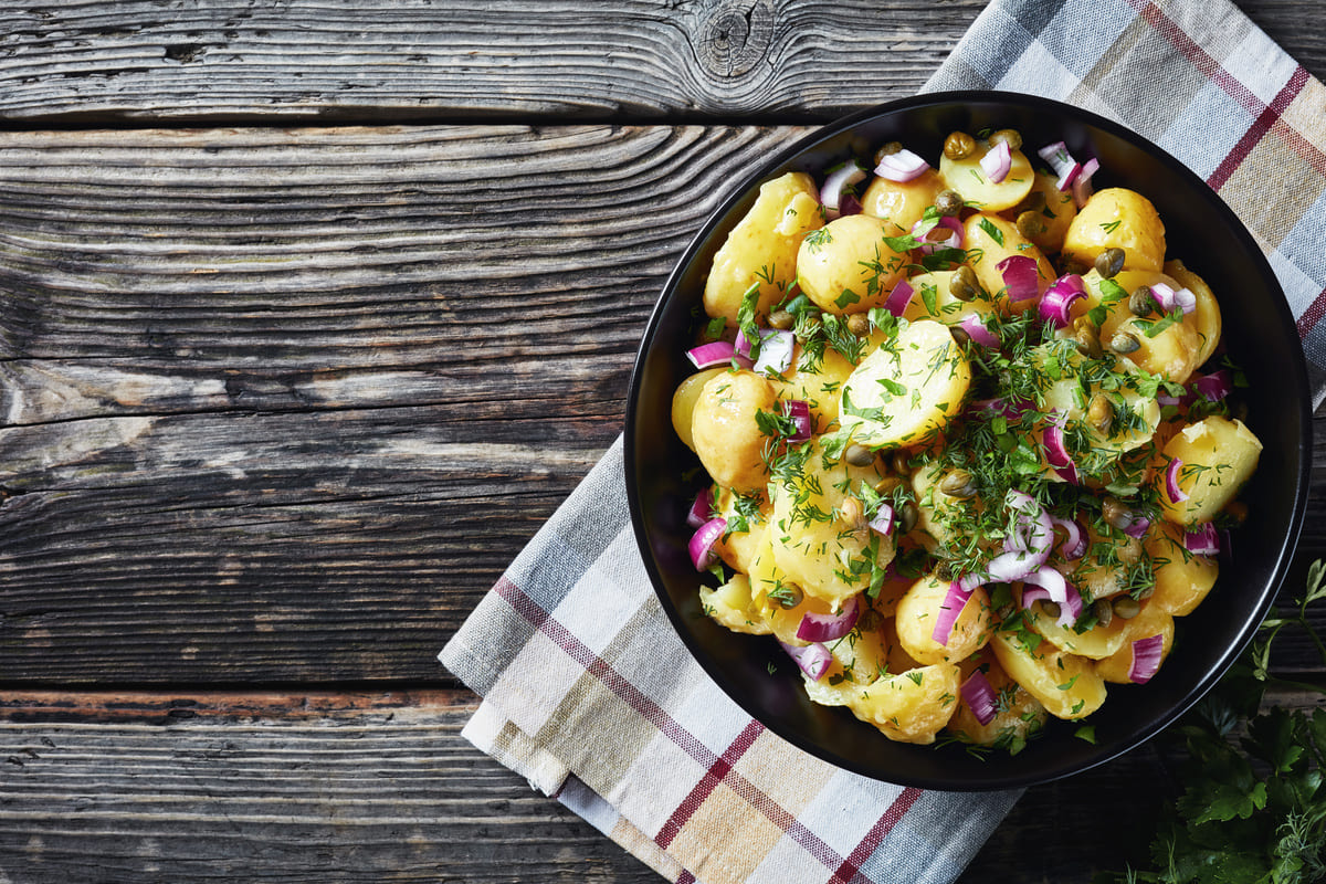 in primo piano su un piatto fondo nero dell'insalata di patate con cipolle rosse e prezzemolo