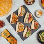Bao buns o gua bao: la ricetta dei panini cinesi al vapore 1 su tavolo di marmo: tagliere nero con 6 bao buns ripieni di verdure, attorno verdure e spezie