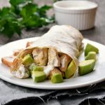 Burrito di pollo con guacamole al lime 1 primo piano di un piatto bianco sul tavolo con burrito di pollo e avocado