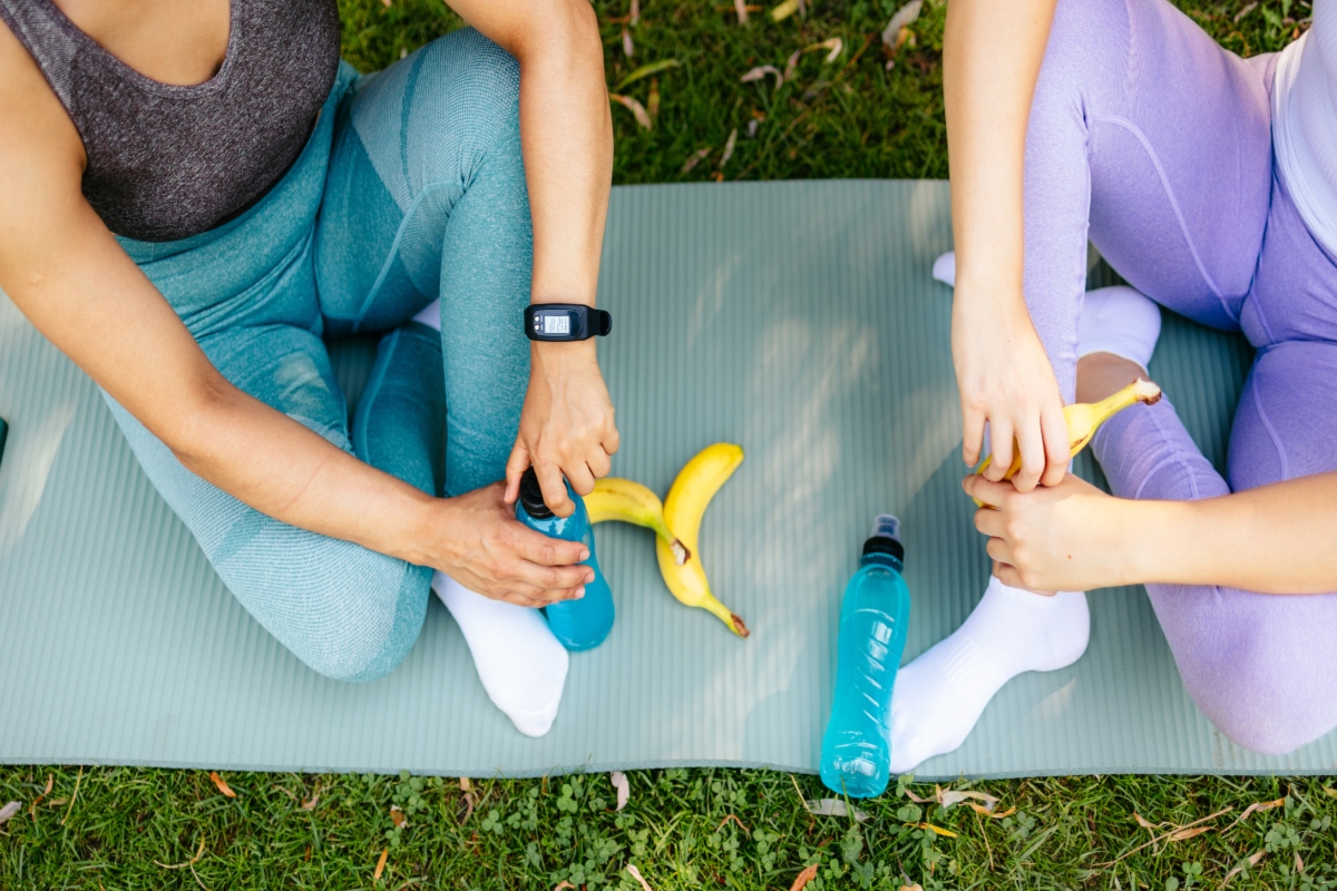 su tappetino gambe di 2 donne sedute dopo sport che parlano. Una tiene la borraccia in mano e l'altra ha in mano una banana