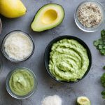 Maionese di avocado: una ricetta sfiziosa 1 su tavolo di marmo, ciotola con la maionese di avovado e attorno tutti ingredienti limone, avocado tagliato in 2 limone, sale, erbe aromatiche