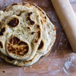 Pane Naan: il pane soffice indiano cotto in padella 1 in primo piano del pane naan su una tavola di legno e un mattarello