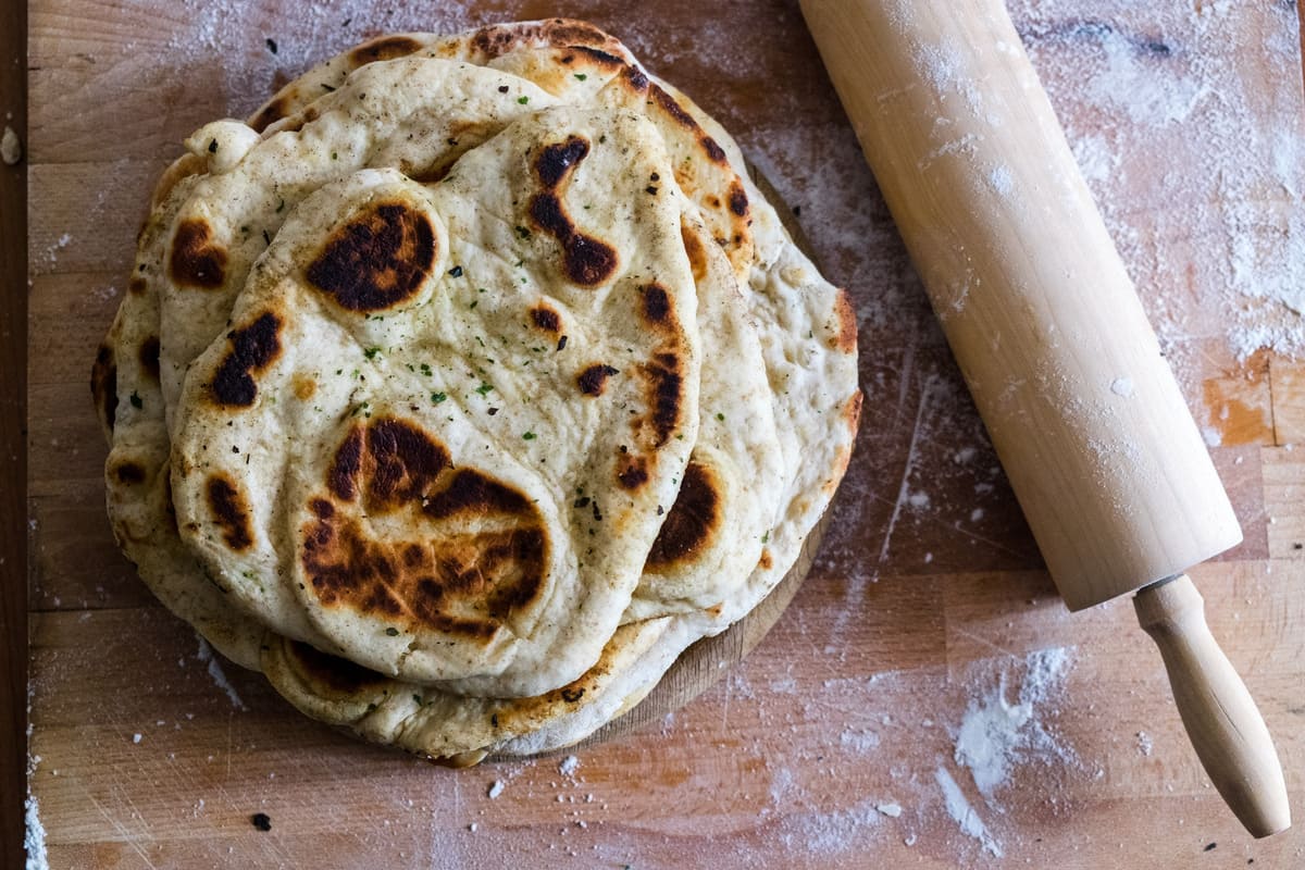 Pane fatto in casa: ricette genuine e semplici da provare 16 in primo piano del pane naan su una tavola di legno e un mattarello