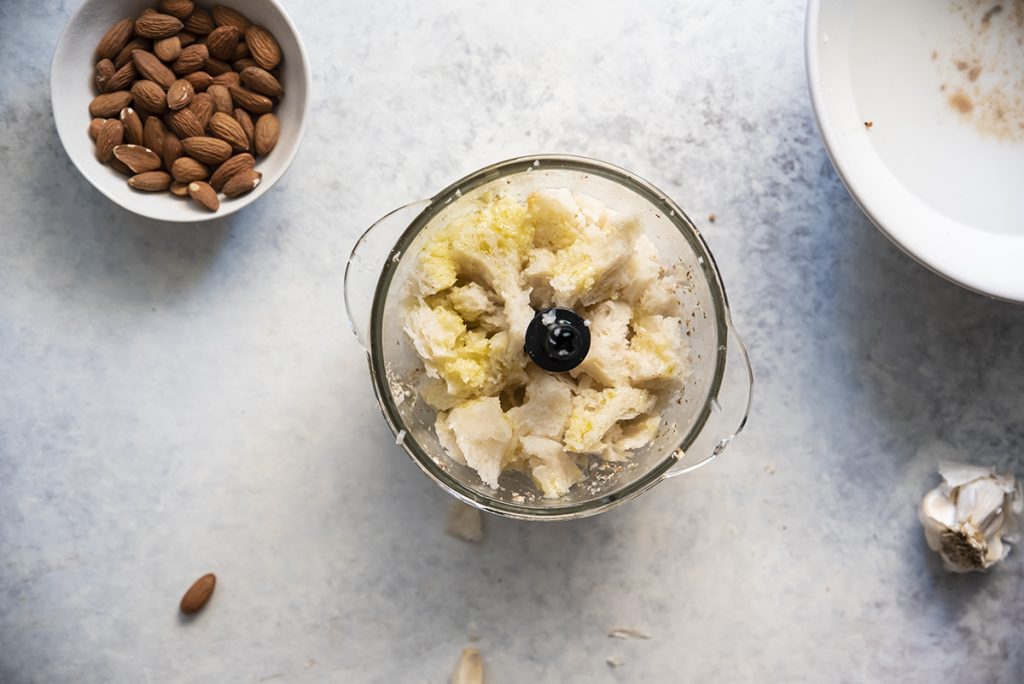 Ajo blanco da Siviglia: una deliziosa zuppa fredda con aglio e mandorle 3 nel frullatore della mollica di pane e accanto una ciotola di mandorle
