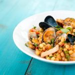 Fregola ai frutti di mare: uno squisito primo piatto sardo 1 su tavolo di legno blu, un piatto bianco con la fregola ai frutti di mare