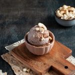 Gelato senza lattosio e senza glutine fatto in casa: ricetta facile per intolleranti 1 su tavolo di marmo tagliere con ciotola e una gelato senza lattosio con granella di cioccolato e mandorle, dietro ciottola con frutta secca