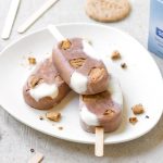 Gelato senza zuccheri aggiunti: ricetta fatta in casa 1 su sfondo bianco, piatto bianco con gelato senza zuccheri aggiunti fatto con i biscotti Céréal senza zuccheri aggiunti. Attorno bastono per gelati e pezzi di biscotti