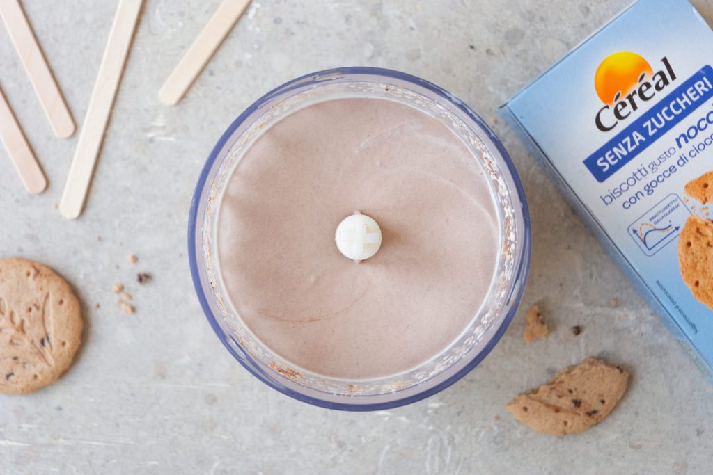 Gelato senza zuccheri aggiunti: ricetta fatta in casa 3 una ciotola tonda con la crema per il gelato dentro, accanto i bastoncini e una confezione di biscotti Céréal