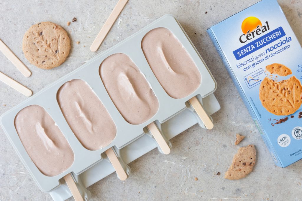 Gelato senza zuccheri aggiunti: ricetta fatta in casa 4 uno stampino per gelati con 4 gelati a stecco in preparazione e una confezione di biscotti Céréal accanto