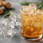 Ginger ale fatto in casa: la ricetta facile del cocktail analcolico 1 Su tavolo da cucina primo piano di un bicchiere con un ginger ale con ghiaccio e accanto cubetti di ghiaccio, zenzero e erbe aromatiche