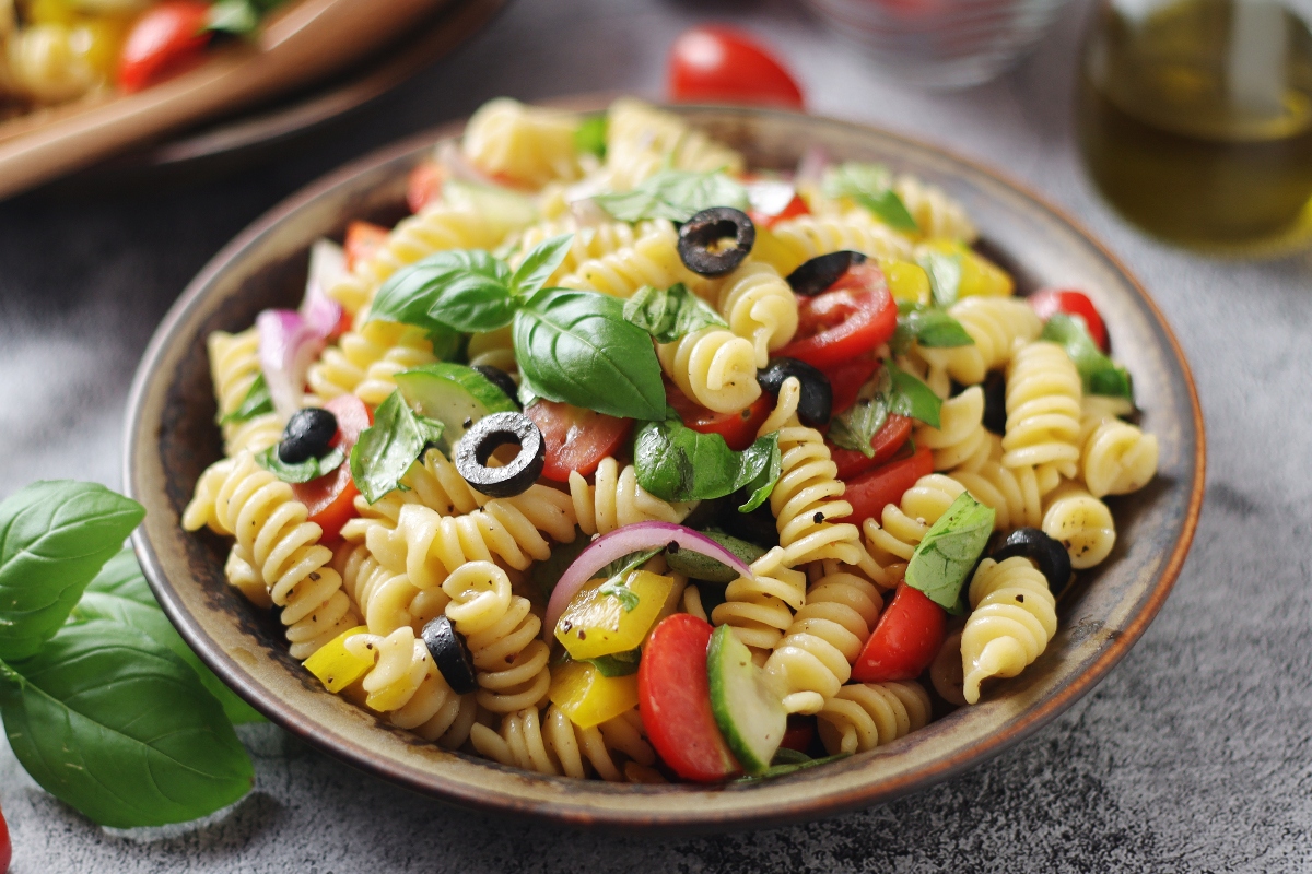 Pasta fredda: 15 ricette veloci da preparare 3 su tavolo da cucina un piatto di pasta alla mediterranea con pomodori, peperoni olive nere e basilico