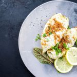 Calamari gratinati al forno: una deliziosa ricetta light e veloce da preparare 1 Calamari gratinati al forno con pangrattato croccante, serviti con fette di limone e foglie verdi su un piatto grigio.