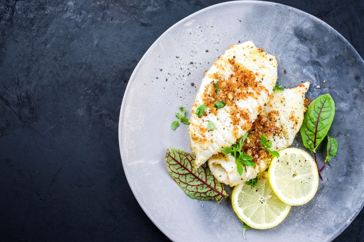 Calamari gratinati al forno con pangrattato croccante, serviti con fette di limone e foglie verdi su un piatto grigio.