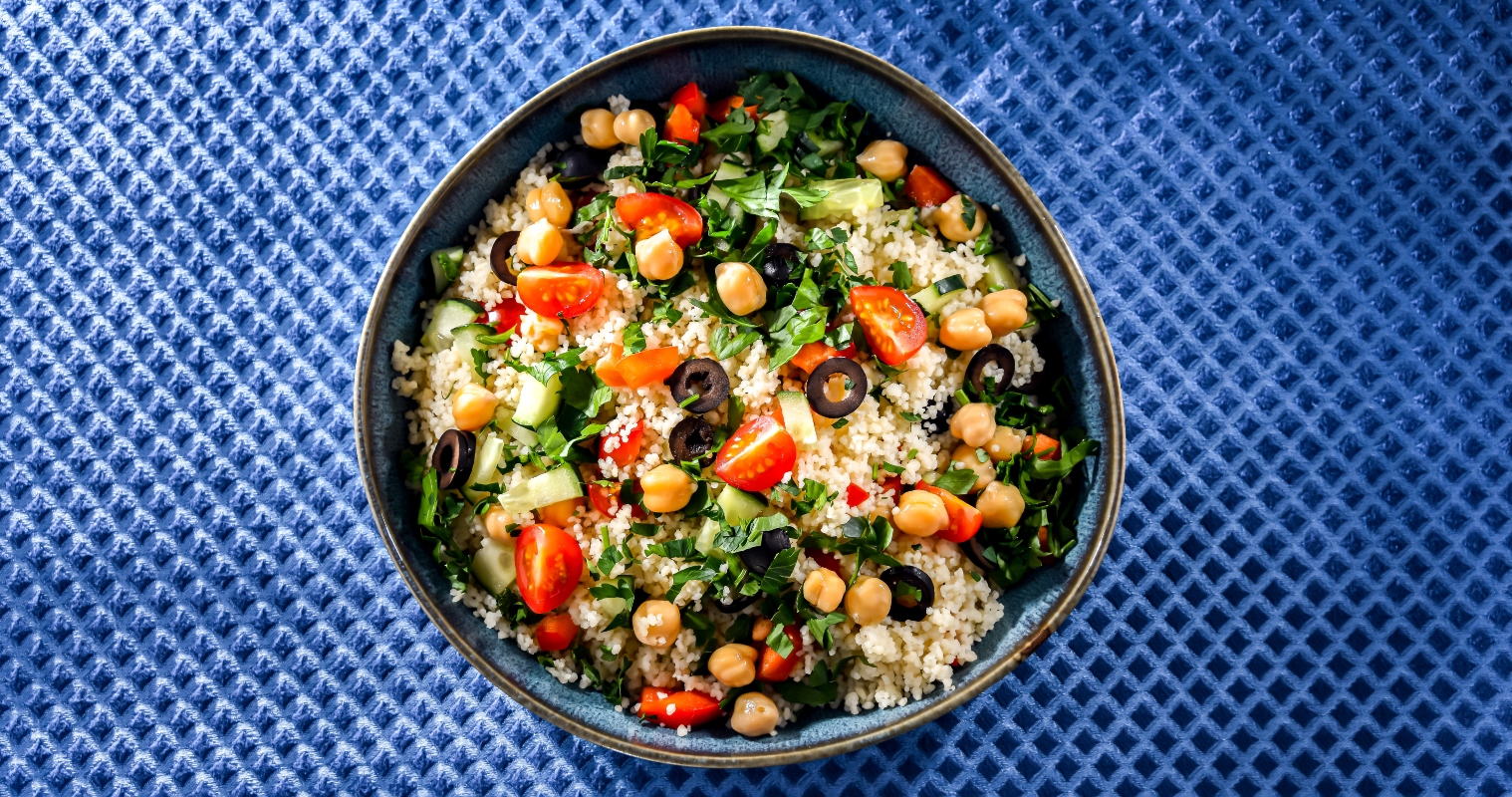 Ricette con cous cous: 10 proposte veloci da provare 3 su sfondo blu una ciotola con insalata di cous cous e ceci, pomodorini, olive nere e insalata