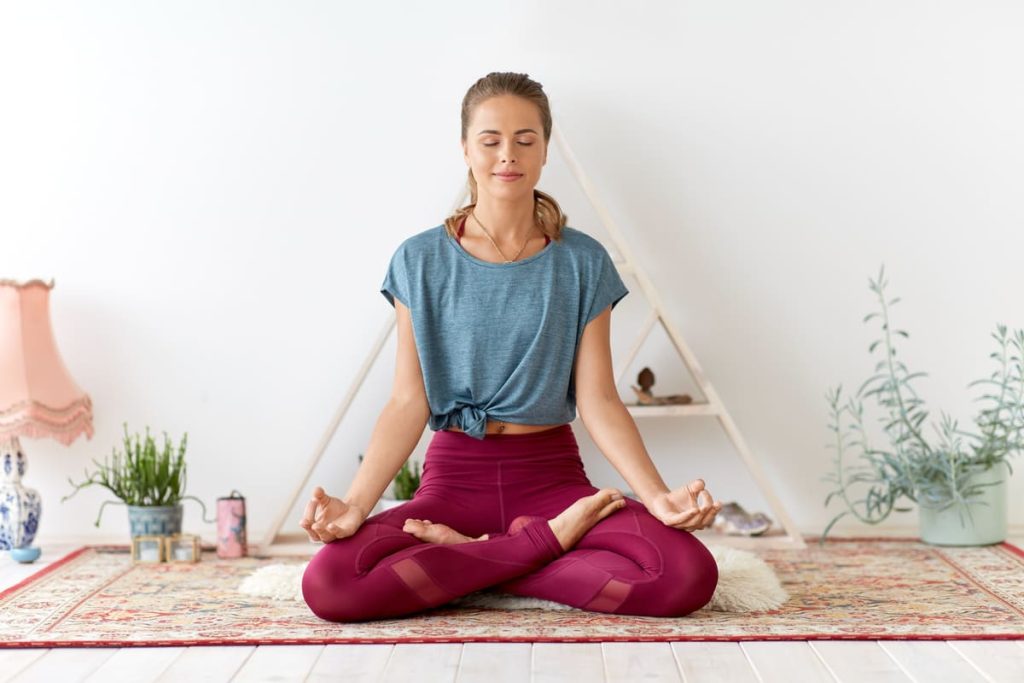 Mindful eating: cos'è, perché fa bene e i 6 passi per cominciare 1 Donna in posizione di meditazione a gambe incrociate che pratica mindful eating e consapevolezza del respiro in un ambiente domestico.