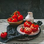Pomodori ripieni di tonno: un delizioso antipasto estivo 1 su tavolo di legno bianco piatto con canovaccio nero a righe bianche e un piatto con pomodori ripieni di tonno in scatola, dietro ciottola con pomodori e dietro una brocca d'acqua bianca su sfondo nero