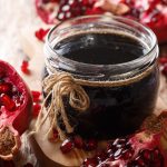Marmellata di melograno senza zucchero fatta in casa 1 su tavolo di legno vasetto con marmellata di melograno e accanto melograna tagliata in 2