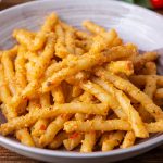 Pesto alla Trapanese: la ricetta originale 1 pesto alla trapanese: su tavolo di legno, primo piatto viola con pasta alla Trapanese e dietro pomodorini