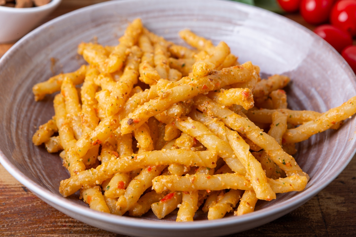pesto alla trapanese: su tavolo di legno, primo piatto viola con pasta alla Trapanese e dietro pomodorini