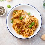 Pesto alla siciliana con pomodori, mandorle e ricotta 1 su tavolo di marmo, piatto bianco con bordo blu spaghetti con pesto alla siciliana e accanto pepe nero in una ciotola e un altra ciotola con sale e foglie di basilico