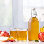 Succo di mela fatto in casa: ricetta senza zuccheri aggiunti 1 In primo piano su un tavolo da cucina ci sono due bicchieri di vetro con del succo di mela. Accanto ci sono delle mele rosse intere e a spicchi e una bottiglia di vetro con il succo.
