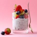Chia pudding: la ricetta del budino di semi di chia 1 su sfondo rosa, in un bicchiere trasparente un chia pudding con semi di chia, frutta tagliata a pezzi, mirtilli, fragole,kiwi