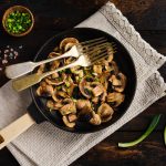 Funghi champignon in padella: la ricetta di un contorno semplice e gustoso 2 In primo piano una padella con funghi champignon in padella, conditi con erba cipollina fresca e accompagnati da sale rosa in granelli.