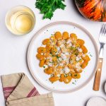 Gnocchi di zucca: condimenti, ricetta base e varianti 1 Piatto di gnocchi di zucca conditi con parmigiano e prezzemolo su sfondo chiaro.