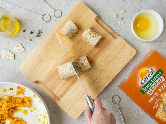 Involtini di zucca e pane azzimo al forno: ricetta e video ricetta di un piatto delizioso 5 su tagliere di legno mano con coltello taglia a metà dei rotolini di pane azzimo